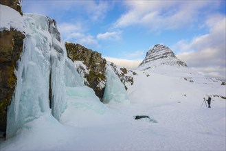 Tourist photographs frozen waterfall Kirkjufellsfoss and mountain Kirkjufell in snow