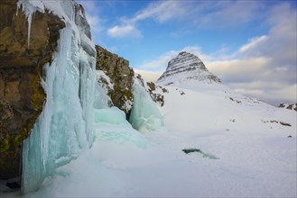 Frozen waterfall Kirkjufellsfoss and the mountain Kirkjufell with snow