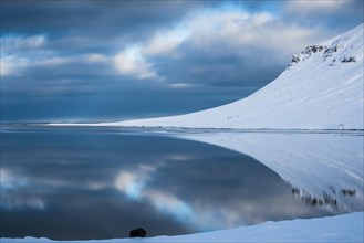 Snow-covered coastal landscape with water reflection