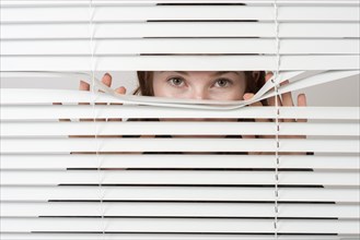 Young woman looking curiously through blinds