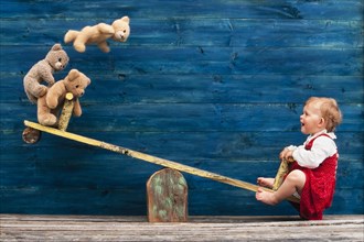 Three-year-old girl with teddy bear on seesaw