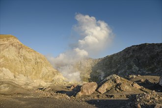 Rock formations and fumaroles on the volcanic island of White Island with rising steam from the crater