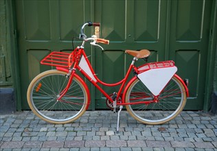 Red bicycle with empty signboard in front of a green gate in Ystad