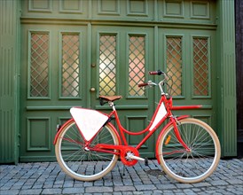 Red bicycle with empty signboard in front of a green gate in Ystad