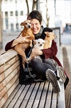 Woman sitting laughing with her three dogs on a bench