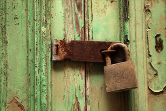 Rusty door lock with deadbolt on weathered wooden door with green paint