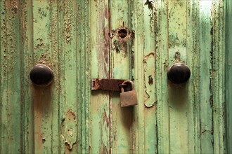 Rusty door lock with deadbolt on weathered wooden door with green paint