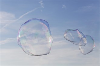Three large soap bubbles in front of a light blue sky