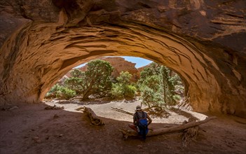 Young man sitting under rock arch