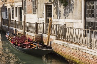 Moored gondola with heart-shaped pillow on narrow canal lined with historical architectural residential buildings