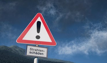 Warning sign against blue sky with clouds