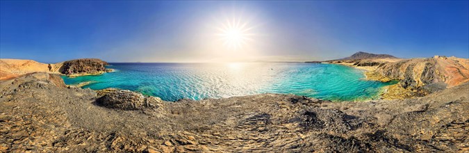 Panorama with sun on rocky coast with turquoise waters of Playa del Papagayo