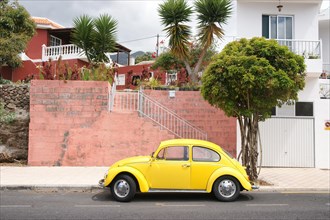 Yellow VW Beetle stands in front of red wall on the Canary Island La Palma