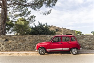 Red Renault R4 stands at a street in front of a stone wall in St. Florent