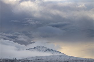 Snow-covered mountain top with clouds in snow-covered landscape