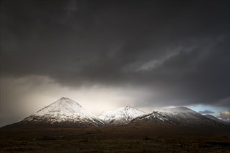 Moor landscape with snow-covered peaks of the Cullins Mountains in front of dramatic clouds in Highland Landscape