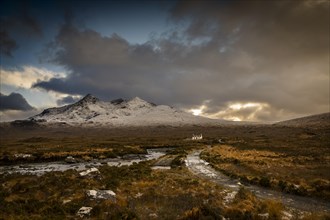 Waterfall of AltDearg Mor with snowy peaks of Marsco and Sgurr Nan Gillean and small house