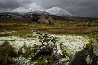 Rock row with white caps and house ruin in Highland scenery with snowy Cullin mountains in the background