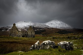 Rocks with white caps and house ruin in Highland landscape with snowy Cullin mountains in the background