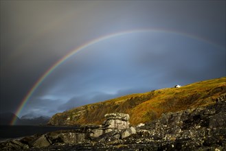 Big rocks in the water of the North Sea with snowy Cullin mountains and rainbow in the background