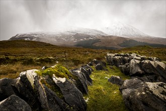 Dark rocks with white caps in Highland landscape with snow-covered Cullin mountains in the background