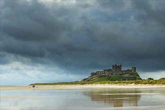 Flat sandy coast with Bamburgh Castle and reflection in the water with dark clouds