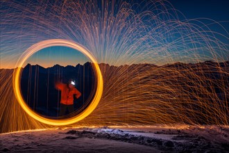 Fire hoop with flying sparks on mountain peaks in front of sunrise