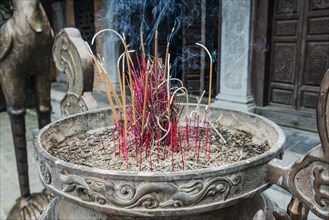 Incense sticks burning in a container in front of a Buddhist temple at Trang An Grottoes in the Trang An Scenic Landscape Complex