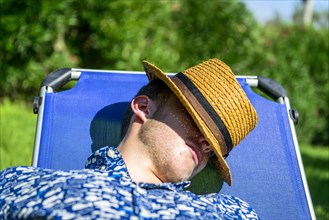Young man with a straw hat sleeping on a sun lounger on holiday