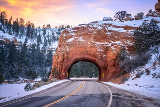 Road with tunnel through red rock arch in snow