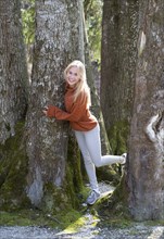 Young woman with long blond hair leaning on a tree