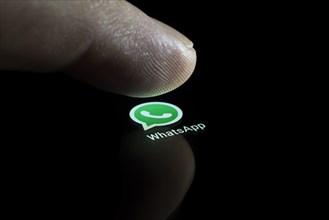 WhatsApp app icon on a display with finger