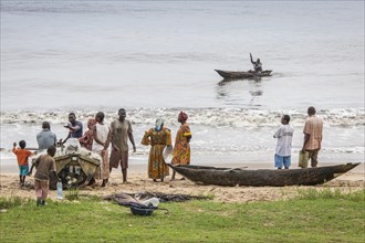 People standing near a dugout canoe on the beach