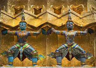 Guardian mythical demons figures or Yaksha supporting the base of a golden Chedi at Wat Phra Kaew