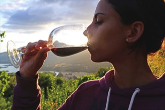 Young woman drinks red wine at sunset