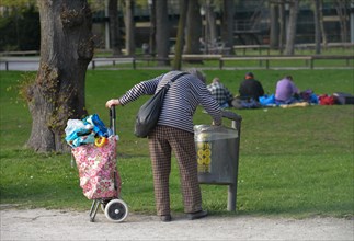 Old woman collects deposit bottles from garbage can