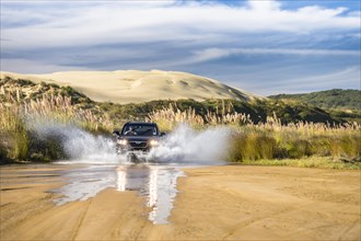 Black Hyundai Santa Fee 4x4 off-road vehicle driving through a streambed on approach to Ninety Mile Beach with sand dune behind