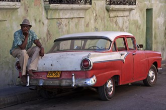 Cuban taxi driver sitting on a vintage taxi car