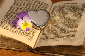 Silver heart and flower of the pansy (Viola) on an open old book