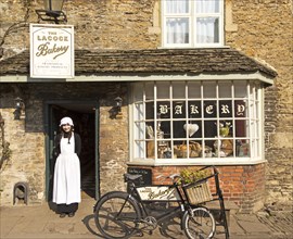Young shopkeeper woman in old fashioned traditional clothing outside the village bakery shop