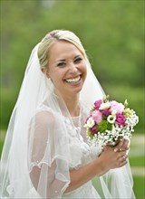 Laughing bride in white wedding dress with bridal bouquet and veil