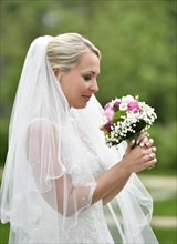 Bride in wedding dress with veil looking at bridal bouqet