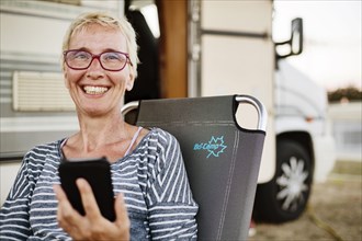 Woman sits with smartphone in a camping chair in front of her camper van