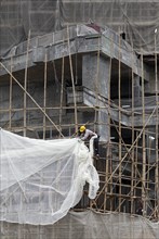 Workers attached a tarpaulin to a scaffolding of bamboo