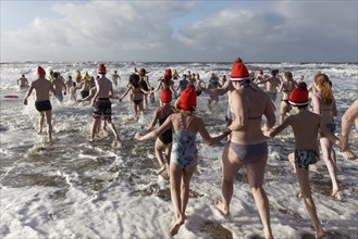 Many people in swimwear and Christmas hats run into the cold sea in winter
