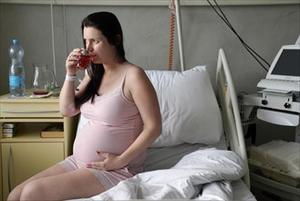 Pregnant woman sitting on sickbed in sickroom