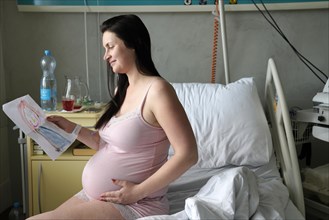 Pregnant woman sitting on sickbed in hospital room with picture of child