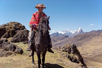 Indio mountain guide with colorful poncho riding on horse in the mountains