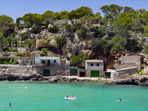 Tourists swim in front of fishing village in the bay of Cala Figuera