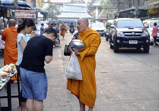 Faithful Thais bow in front of a begging monk